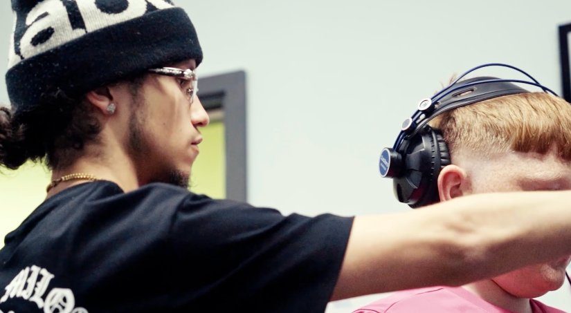 Mentor adjusting headphones for a young person before recording